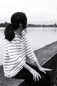 Girl sitting on retaining wall against lake