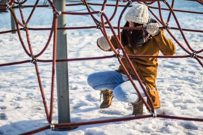 Full length of woman crouching under ropes at snow covered park