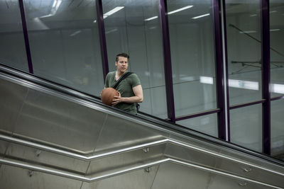 Man with basketball standing on escalator