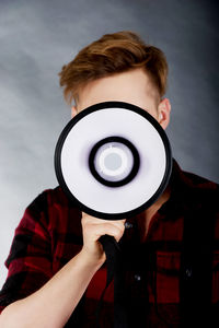 Young man with megaphone standing against gray backdrop