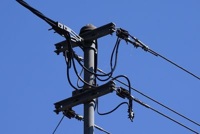 Low angle view of electricity pylon against clear blue sky