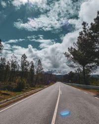 Empty road along trees and against sky