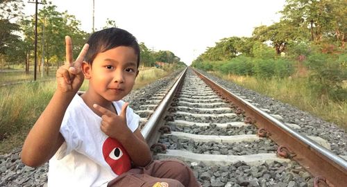 Portrait of boy gesturing peace sign while sitting on railroad track