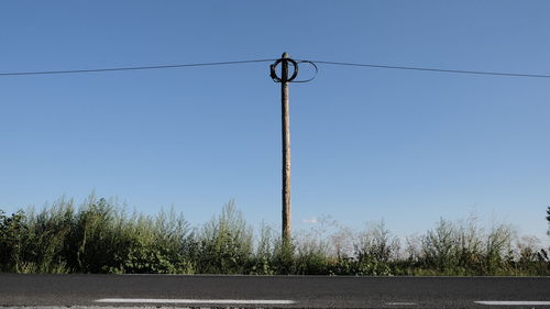 Low angle view of electricity pylons against clear blue sky