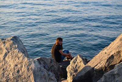 Young woman sitting on rock by sea
