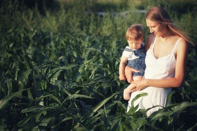 Mother with baby boy in arms on green cultivated field