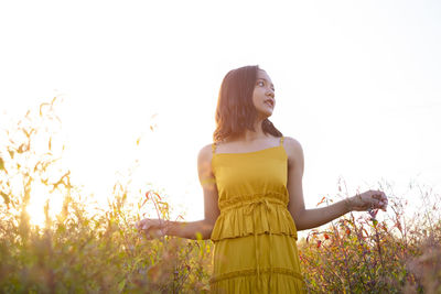 Young woman standing on field against sky