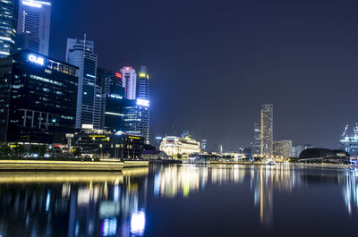 Illuminated buildings by river against sky at night