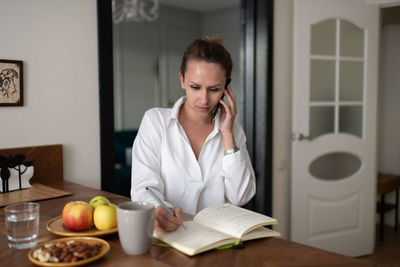 Businesswoman speaking on smartphone and making notes