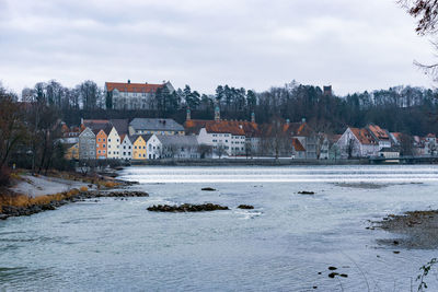 Buildings by river against sky during winter