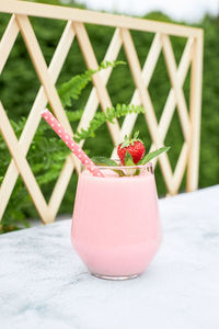 Strawberry smoothie or milkshake with banana and mint in a glass glass on a table in the garden. 
