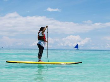 Full length of woman paddle boarding on sea against cloudy sky