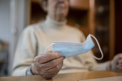 Hand of wrinkled woman holding protective face mask during lockdown at home