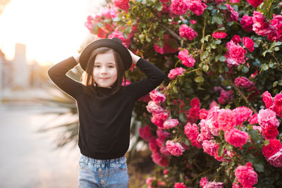 Smiling kid girl 4-5 year wearing stylish clothes posing over rose flowers at background closeup.