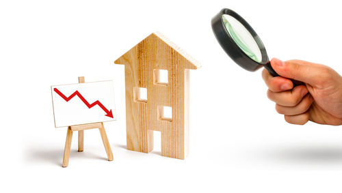 Magnifying glass is looking at the wooden house and red arrow down. concept of falling prices 