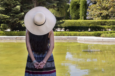 Rear view of woman wearing hat standing by lake