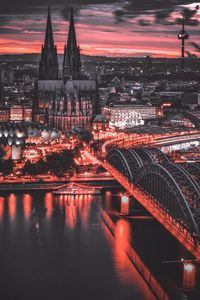 Illuminated bridge over river in city at dusk