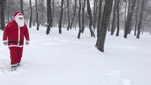 Man wearing santa claus costume walking against trees on snow covered field