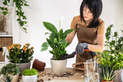 Side view of young woman holding potted plant at home