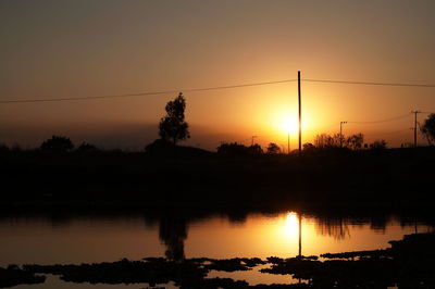 Silhouette trees by lake against sky during sunset