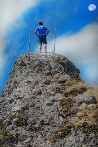 Rear view of man standing on rock formation against sky