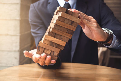 Close-up of businessman holding jenga blocks on table