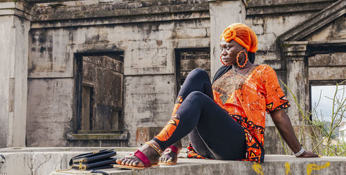 Africa woman sits wearing an orange suit on a concrete wall in takoradi ghana west africa.
