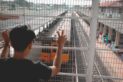 Rear view of man standing by metal fence