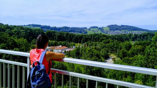 Rear view of woman standing by railing against green landscape