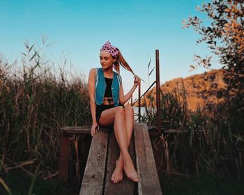 Full length of young woman sitting on plank against sky