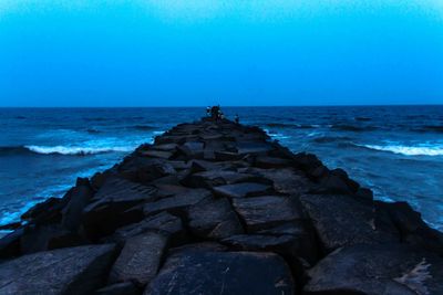 Man standing on rock by sea against clear blue sky