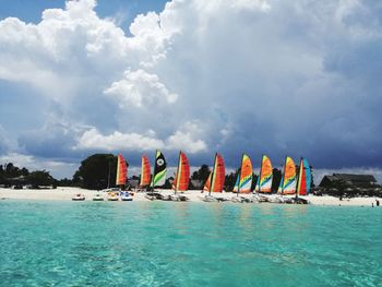 Sailboats sailing in sea against cloudy sky