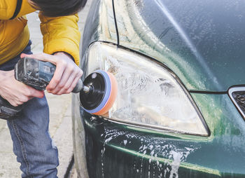 The hands of a guy are drilling with a sponge and polishing the headlight