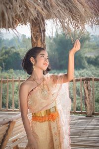 Girl in traditional clothing standing by thatched roof