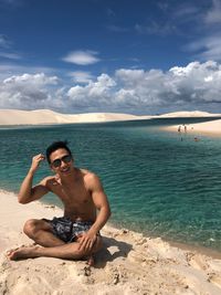 Young man sitting at beach against sky