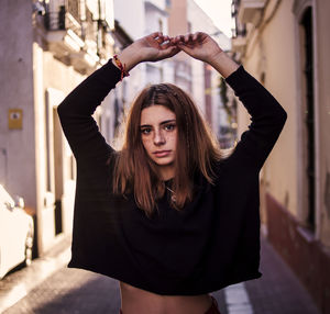 Portrait of young woman standing amidst buildings at alley in city