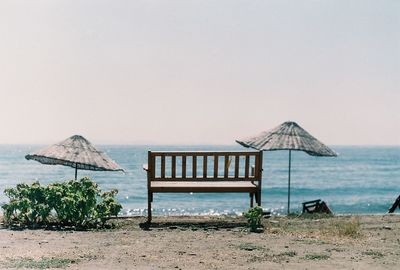 Empty bench on calm beach against clear sky