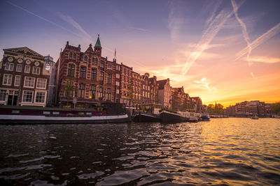 Buildings by river against sky during sunset