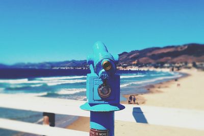 Close-up of coin-operated binoculars at beach against blue sky