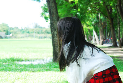 Rear view of woman bending by tree trunk in park