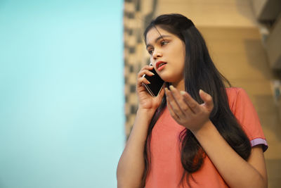 Young woman applying make-up against wall