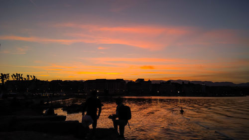 Silhouette people standing on beach against sky during sunset