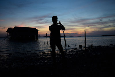 Silhouette man standing at beach against sky during sunset