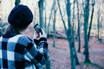 Rear view of woman photographing through mobile phone in forest