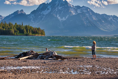 Man standing on rocks by sea against mountains