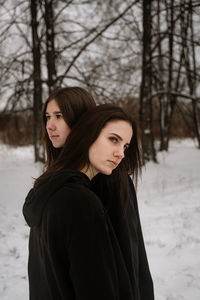 Young women looking away while standing on snow covered land