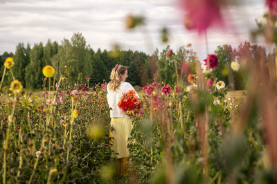 A girl in rubber boots collects autumn flowers on the field