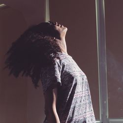 Side view of woman tossing hair while standing against window