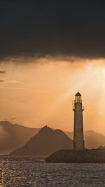 Lighthouse by sea against sky during sunset