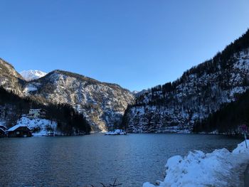 Scenic view of river by snowcapped mountains against clear blue sky